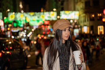 Obraz premium Young woman is walking at night holding a coffee in a city center street decorated for christmas