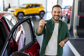 Handsome man raising hand up with the car key and smiling at camera, showing key from his brand new...