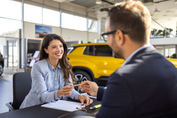 Beautiful woman Buying New Car Signing Papers With Dealer Man Standing In Auto Dealership Store.