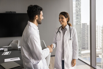 Young man woman medics coworkers shake hands after successful partnership collaboration. Happy...