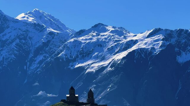 Trinity Church of Gergeti on the background of snow-capped mountains. View of the mountain peaks near Stepantsminda, Georgia. The ancient Christian church of Gergeti at the foot of Mount Kazbek. 4К