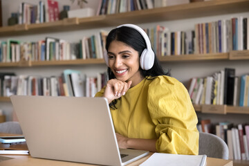 Happy young Indian online student girl in headphones watching learning webinar, online lesson on...