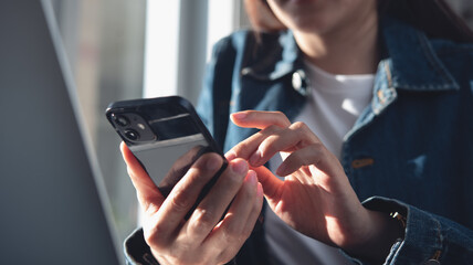 Closeup, business woman sitting at table using mobile smrt phone during working on laptop computer at home office. Young asian woman freelancer  surfing the internet, online working from home
