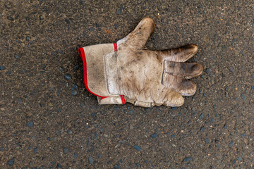 A worn work glove lies on a patch of asphalt