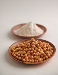 Chickpeas and chickpea powder arranged on a wooden plate, isolated against a clean white background