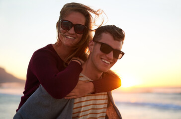 Couple, piggyback and portrait at beach for sunset, relax and tropical holiday together with sunglasses. Man, woman and travel by ocean for fun, romance and summer vacation with weekend date in Ibiza