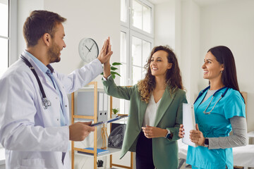 Friendly doctor with nurse rejoicing at success in treatment giving high five to smiling woman...
