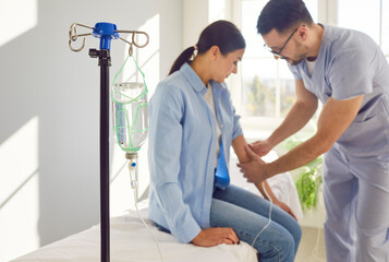 Nurse setting up IV line for patient. Close up glass drip bottle on stand in hospital ward, with...