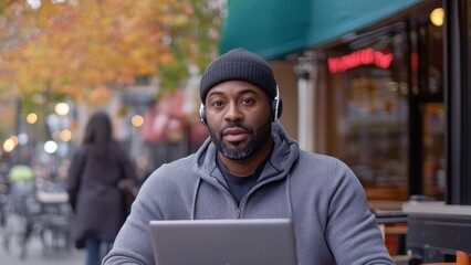 Fototapeta premium A man sits outdoors with a laptop, wearing headphones, engaged in work or leisure.
