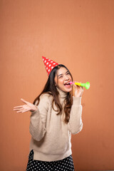 A joyful woman in a colorful party hat celebrates at a fun gathering with a whistle