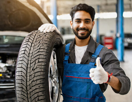Mechanic holding a tire and giving a thumbs up inside an automotive workshop
