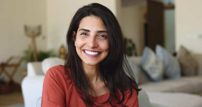 Close up front view face of beautiful authentic Brazilian woman having attractive appearance white perfect smile looking at camera, resting alone in living room. Dental services, home rest, portrait
