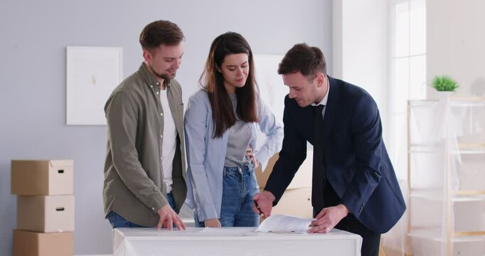 Realtor and young couple flat paper plan showing, small family and agent helping clients buy, rent home, apartment, room. Real estate agent advertising, assisting buyers marketing, display documents