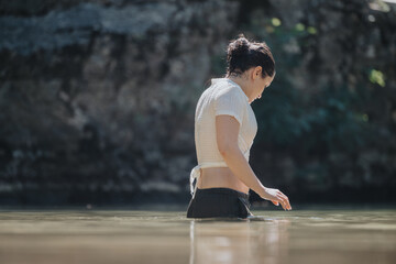A young woman stands in calm water, enjoying a tranquil moment in nature. She is relaxed and immersed in the serene environment, conveying peace and reflection.