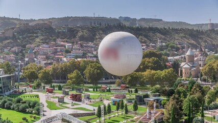 Rike Park from above. Modern urban park in the old town of Tbilisi aerial timelapse. Green trees and lawn at relaxing area in the city. Hot air balloon and cable car. Georgia - Powered by Adobe