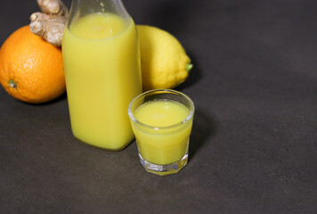 Top view of homemade orange, lemon and ginger drink in a glass bottle with a small shot glass 
