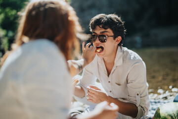 Obraz premium Group of friends at a picnic by the river, sharing food and enjoying the sunny outdoors. Laughter and joy fill the moment as they relax together.