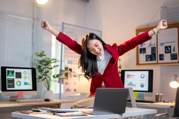 A woman in a red jacket is celebrating with her hands in the air