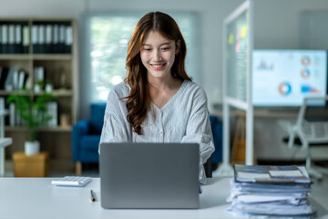 A woman is sitting at a desk with a laptop and a stack of papers