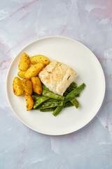 Delicious baked cod fillet served with seasoned potatoes and green beans on a white plate