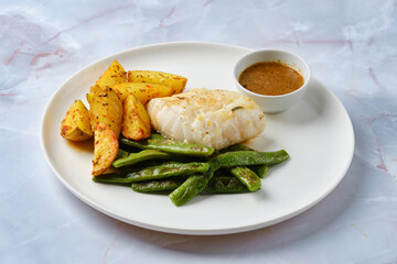 Delicious baked cod served with green beans and golden roasted potato wedges on a white plate