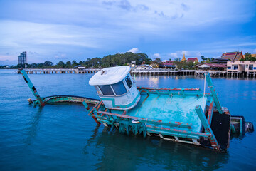 Chonburi, Thailand - May, 26, 2024 : Abandoned Fishing Boat Sinking in Harbor in sunset at...