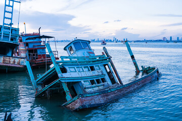 Obraz premium Chonburi, Thailand - May, 26, 2024 : Abandoned Fishing Boat Sinking in Harbor in sunset at Chonburi, Thailand