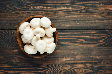 Overhead view of fresh white champignon mushrooms in a wooden bowl on a rustic wooden table