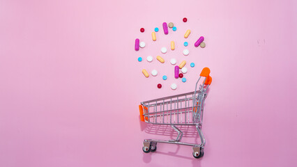 Capsules, pills are scattered out from trolley shopping cart on pink background. Concept for shopping and purchasing. Medical science, medicine, health insurance. Pharmacy, Drugstore.