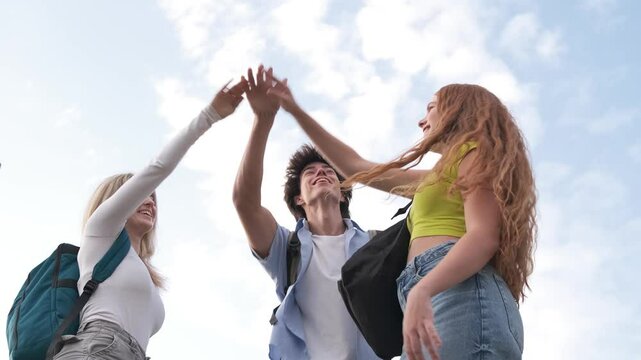 Students stacking hands for teamwork against cloudy sky