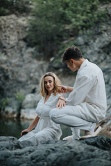 Obraz premium Couple enjoying a serene moment by the river. They are both dressed in white outfits, surrounded by nature
