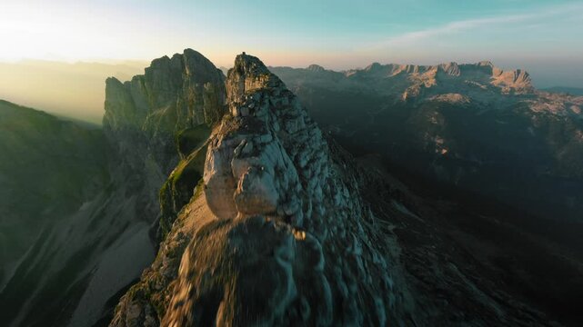 Stunning FPV flight above sunrise mountain ridge orbiting around mountain hut in alps