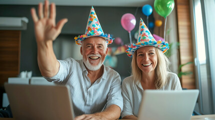 Happy senior couple in party hats waving during a virtual celebration with colorful balloons and decorations in the background