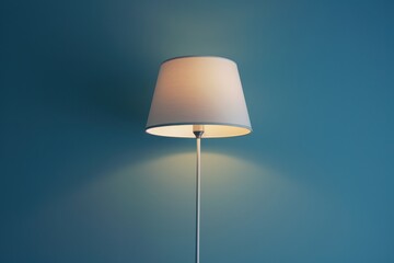 Simple white lamp standing against a blue wall illuminating the room softly