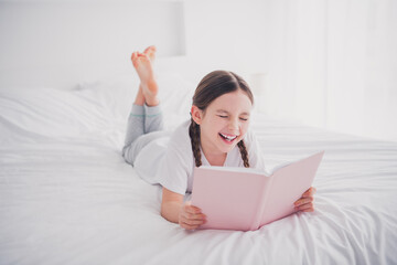 Portrait of cute positive nice girl lying reading interesting book cozy bedroom flat white light...