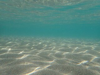 Dark blue ocean surface seen from underwater. Abstract waves underwater and rays of sunlight shining through, Sun light rays undersea deep, Underwater background with sea bottom, Mediterranean sea.