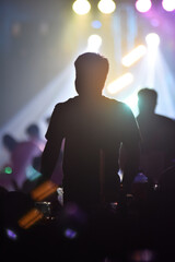 Back view of crowd of people dancing at concert. Silhouette of man in night music dance party.