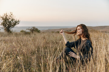 Serene woman sitting in tall grass with windblown hair, watching the sunset in a peaceful field