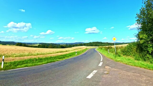 kurvige Landstra&szlig;e durch sanfte H&uuml;gellandschaft im Sommer mit blauem Himmel, l&auml;ndlich, Verkehr, Stra&szlig;e, Vorfahrt, Verkehr, Fahrschule, Verkehrsregeln
