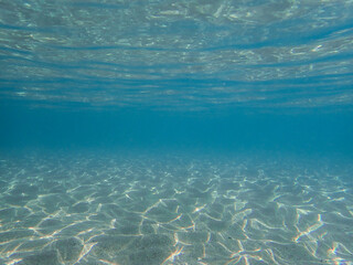 Dark blue ocean surface seen from underwater. Abstract waves underwater and rays of sunlight shining through, Sun light rays undersea deep, Underwater background with sea bottom, Mediterranean sea.