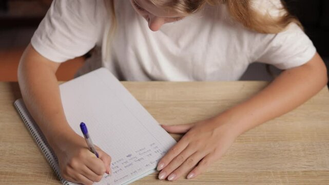 Young student practicing cursive handwriting by repeatedly writing letters in notebook, emphasizing skill development and literacy within classroom environment