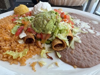 closeup of taquitos topped with salsa, guacamole and sour cream with rice and refried beans - delicious Mexican food