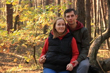 Fototapeta premium A couple sits together outside in an autumn forest on a sunny day, man and woman
