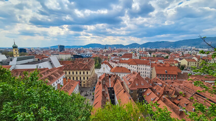 Fototapeta premium Scenic aerial view of Graz seen from Schlossberg, Styria, Austria, Europe. Unesco world heritage site with red-roofed buildings. City is nestled amidst rolling hills. Mur River winds through old town