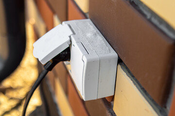 Outdoor electrical outlet on the wall of brick house. Snow and ice on the outdoor outlet. The...