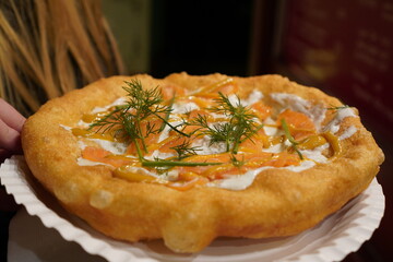 Close up of a langos, typical Hungarian food specialty, with sour cream and fish salmon on a white dish on a brown table, deep fried dough at a christmas market