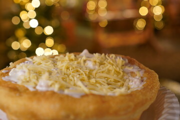 Close up of a langos, typical Hungarian food specialty, with sour cream and cheese on a white dish in hand, deep fried doughin front of christmas lights at a christmas market