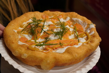 Close up of a langos, typical Hungarian food specialty, with sour cream and fish salmon on a white dish on a brown table, deep fried dough at a christmas market