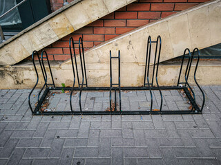 A black bike rack is sitting on the sidewalk next to a brick wall. The rack is empty and has no bikes on it