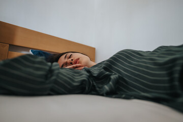A woman peacefully sleeping in a bed, wrapped in cozy striped blankets. The serene atmosphere...